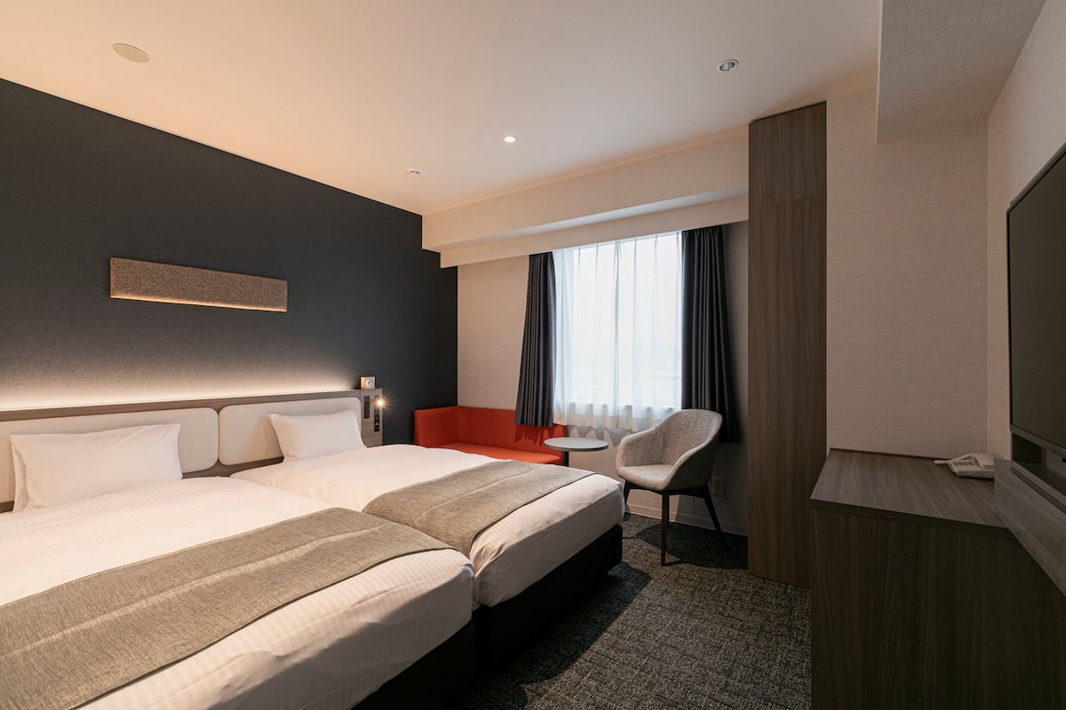 A hotel room with two beds, a desk, a chair, and a television.
