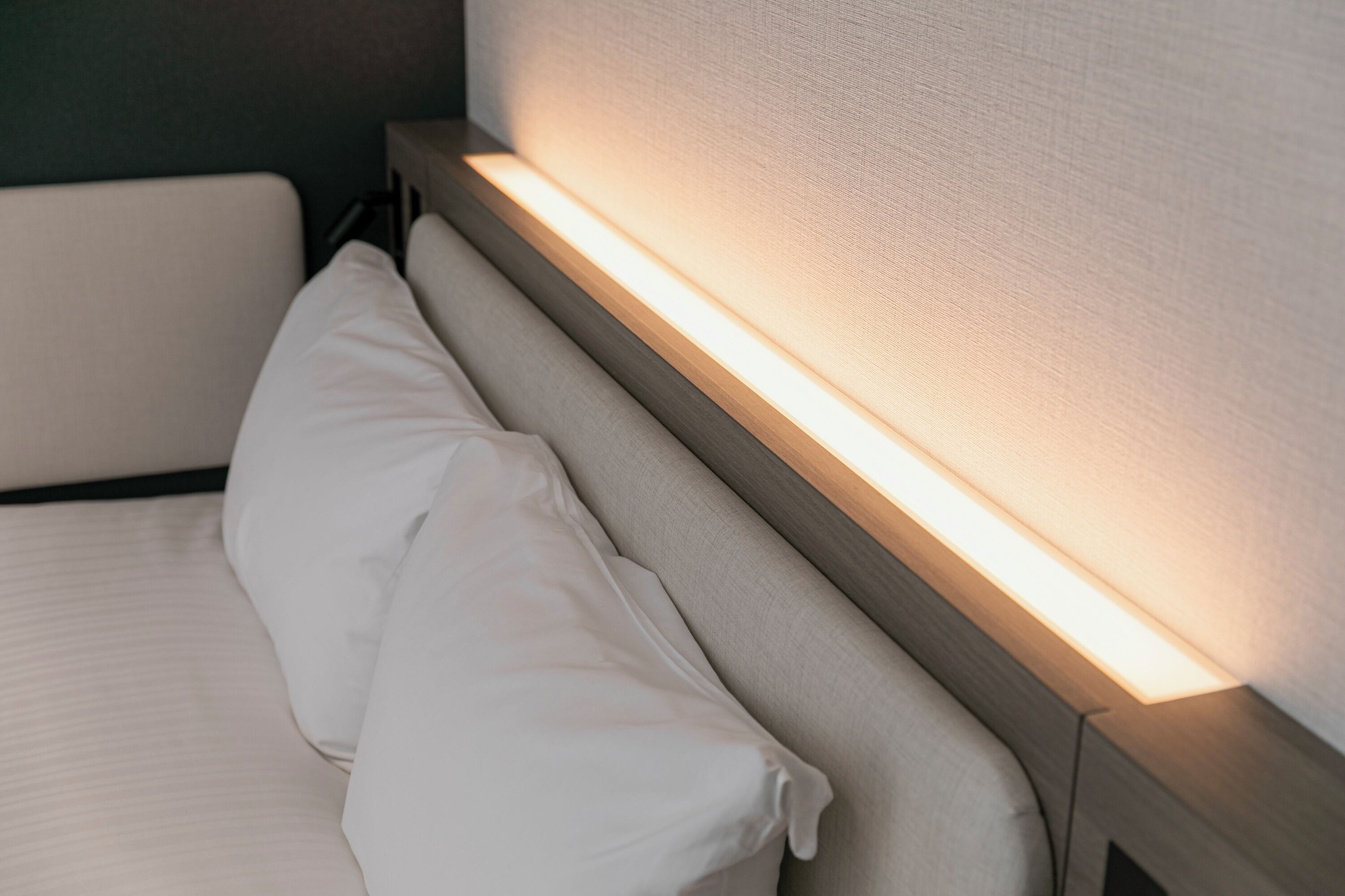 A neatly made bed with white linens and a headboard with integrated lighting.
