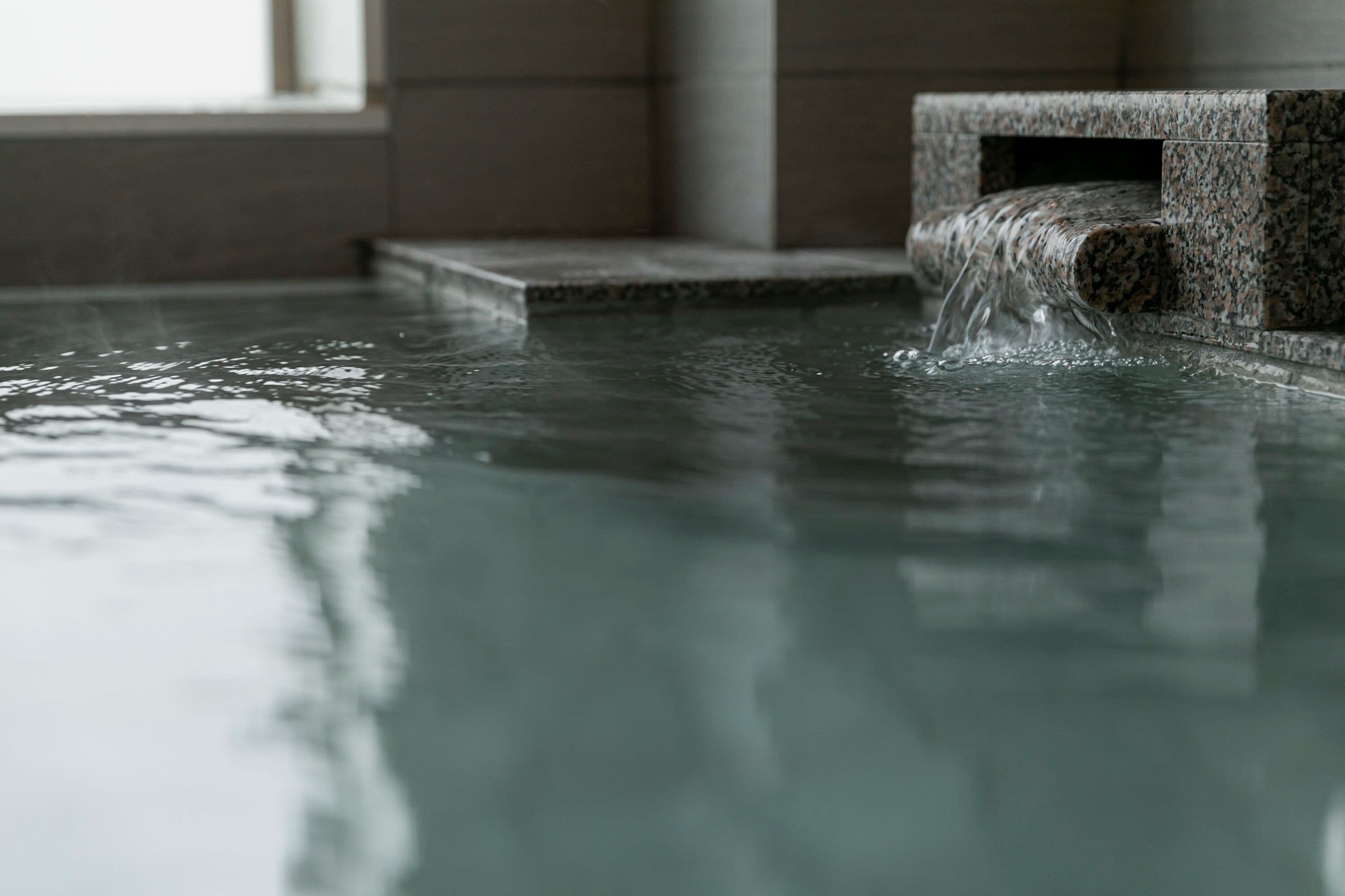 A water feature in a spa area with a stone structure and a window in the background.