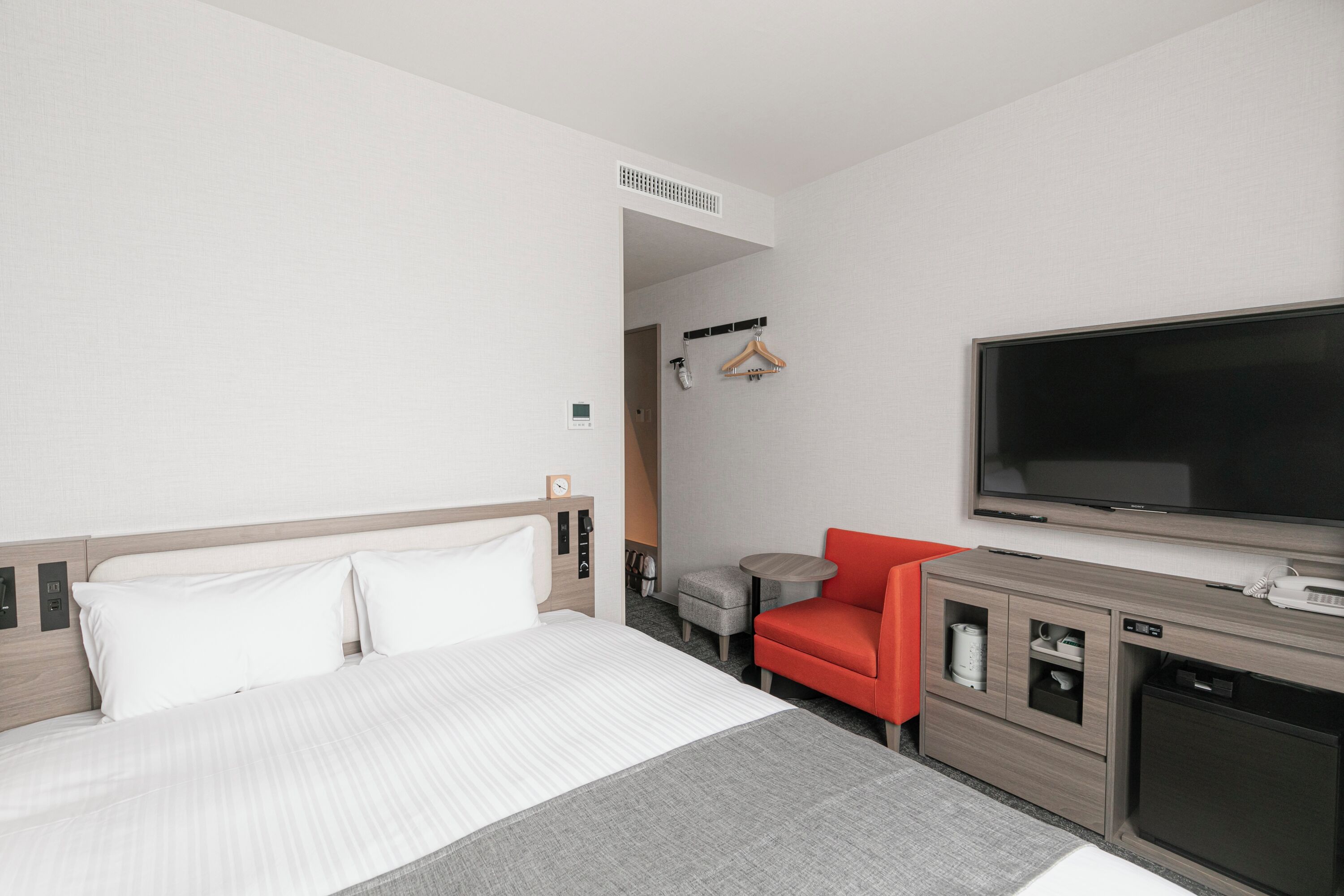 A hotel room with a bed, a television, a red chair, a small table, and a cabinet.