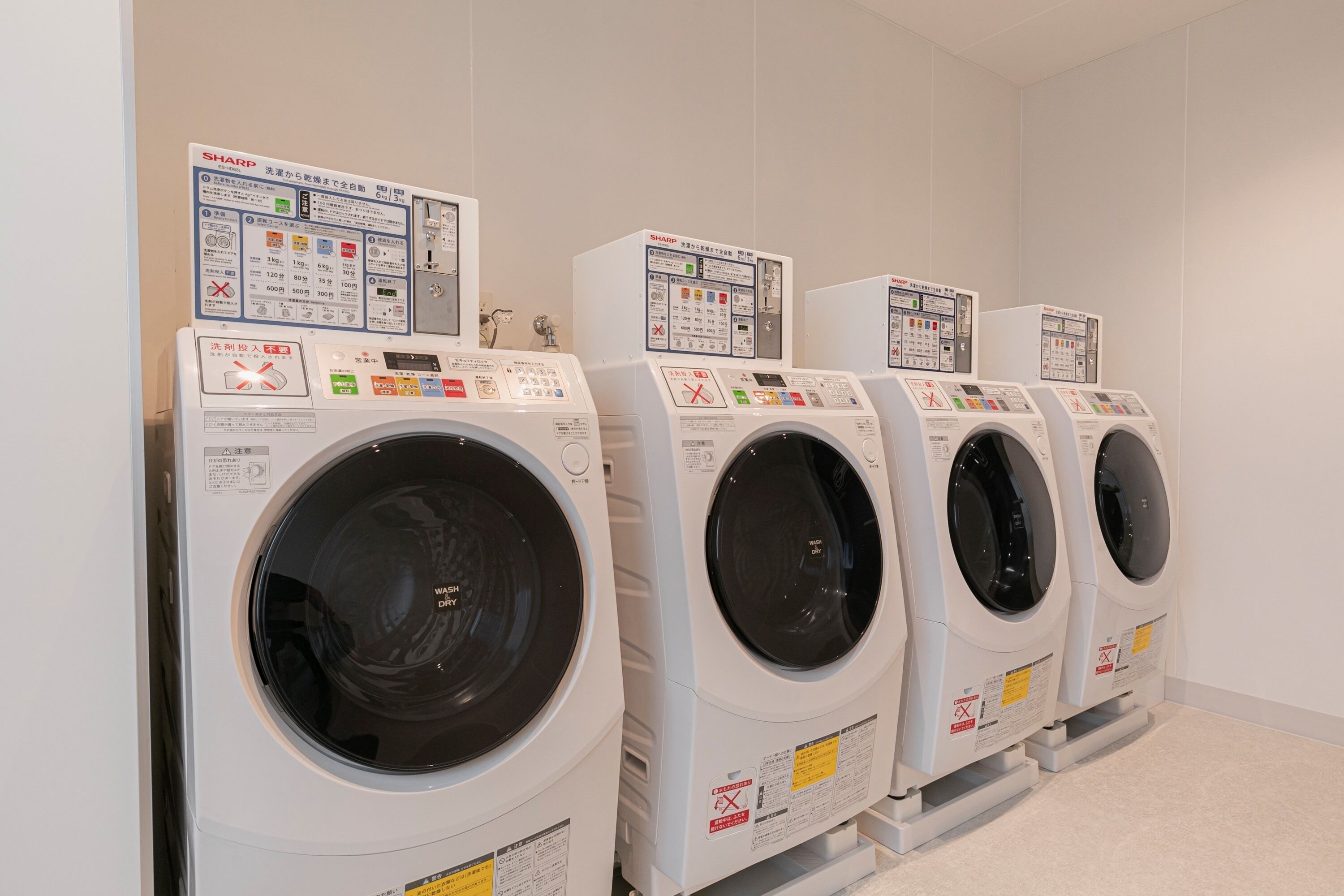A row of white front-loading washing machines with control panels, arranged in a commercial laundry room.