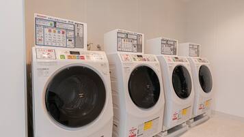 A row of white front-loading washing machines with control panels, arranged in a commercial laundry room.