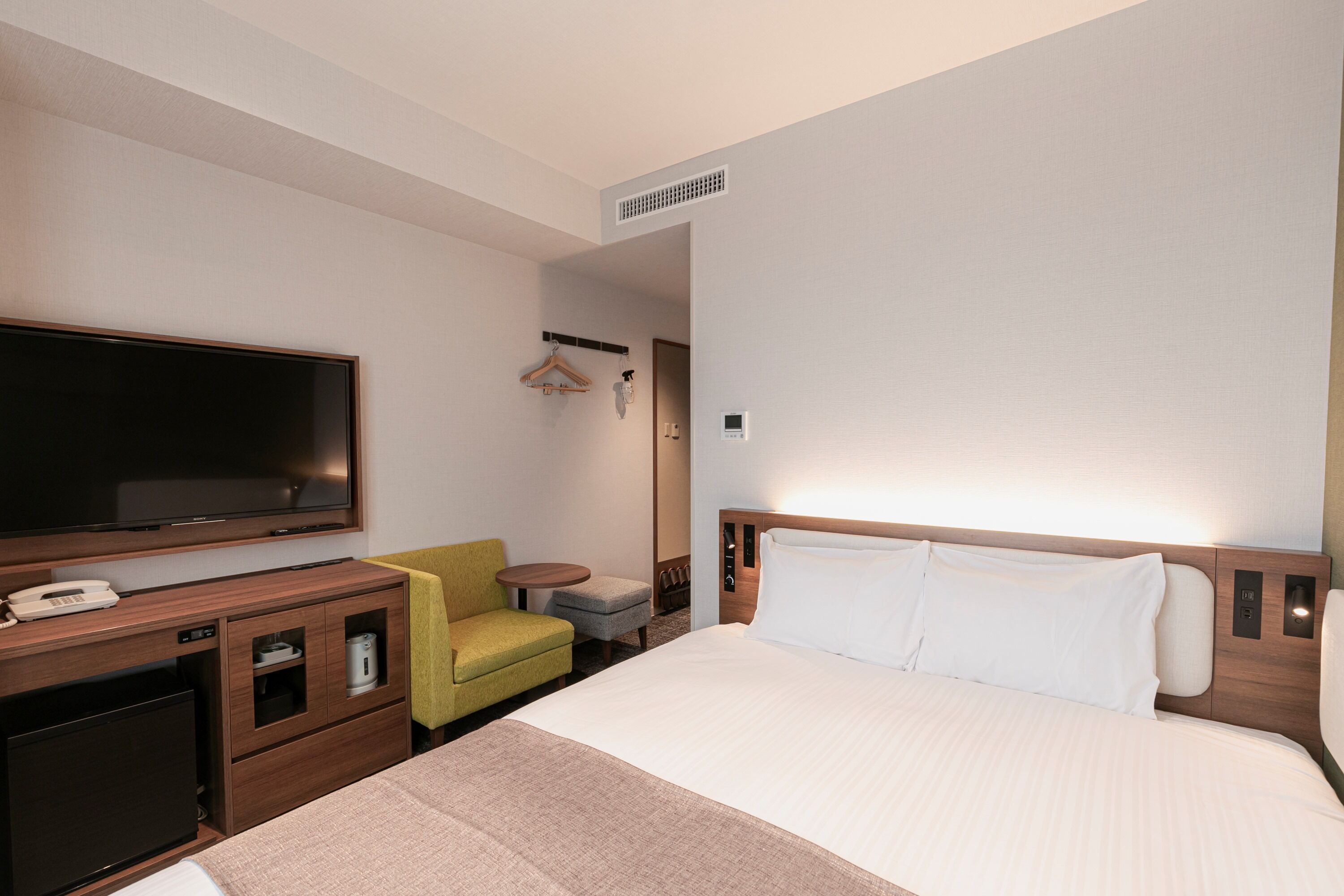 A hotel room with a bed, a TV, a desk with a phone, a chair, and a small table.