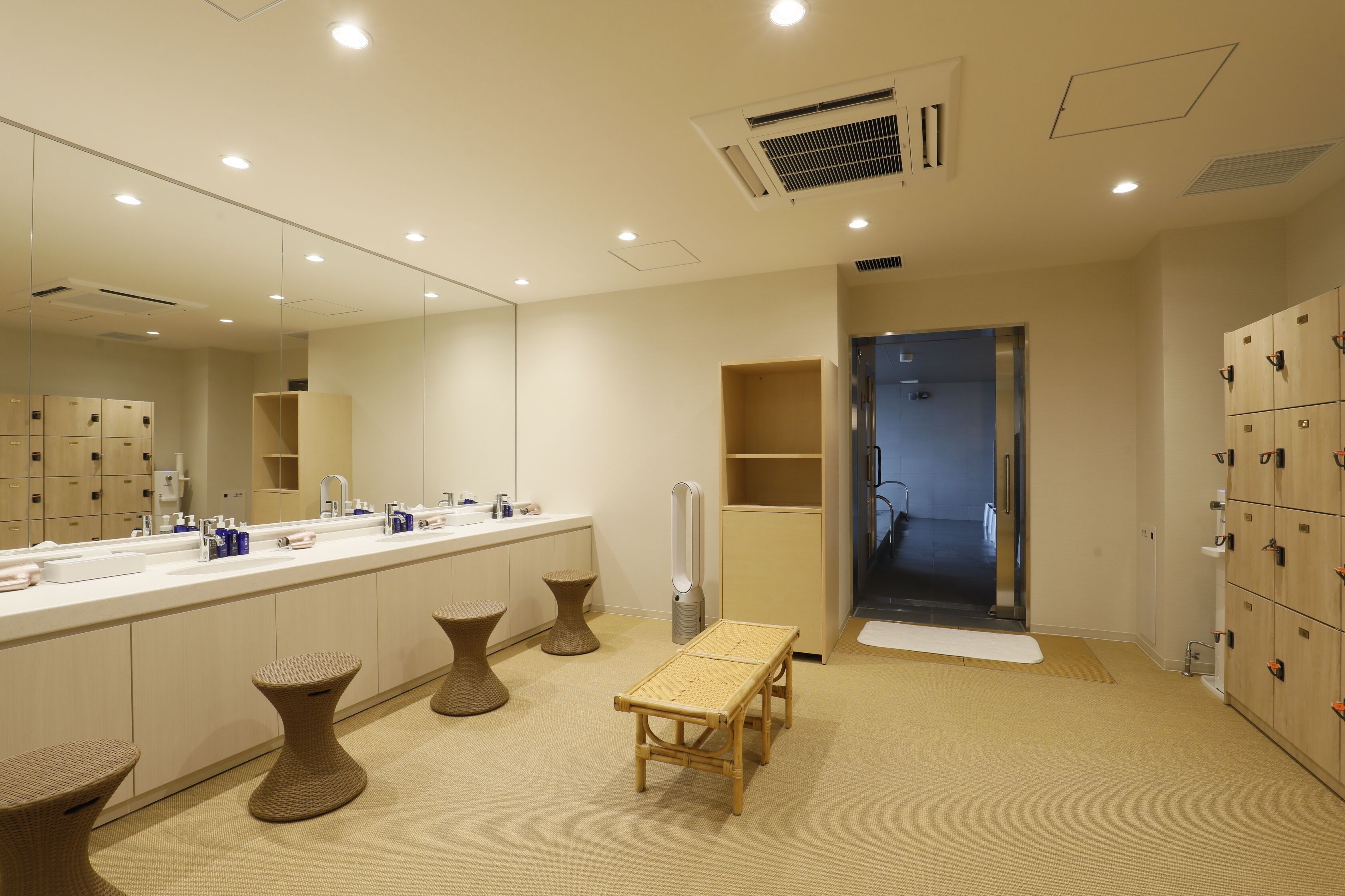 A modern bathroom with a large mirror, multiple sinks, and a bench.