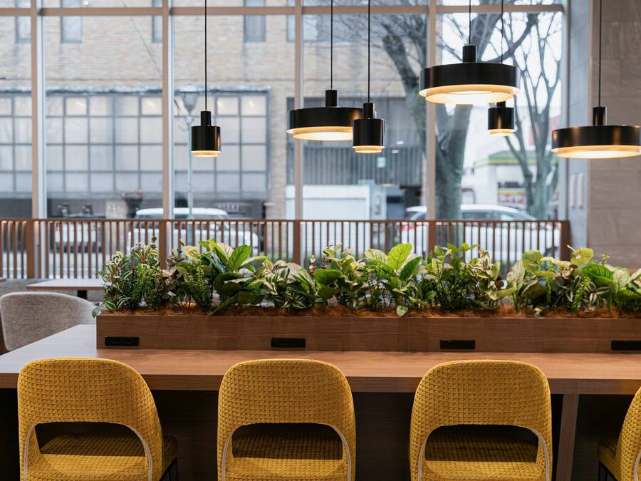 Un espacio interior moderno con una larga mesa de madera, sillas amarillas e iluminación colgante.