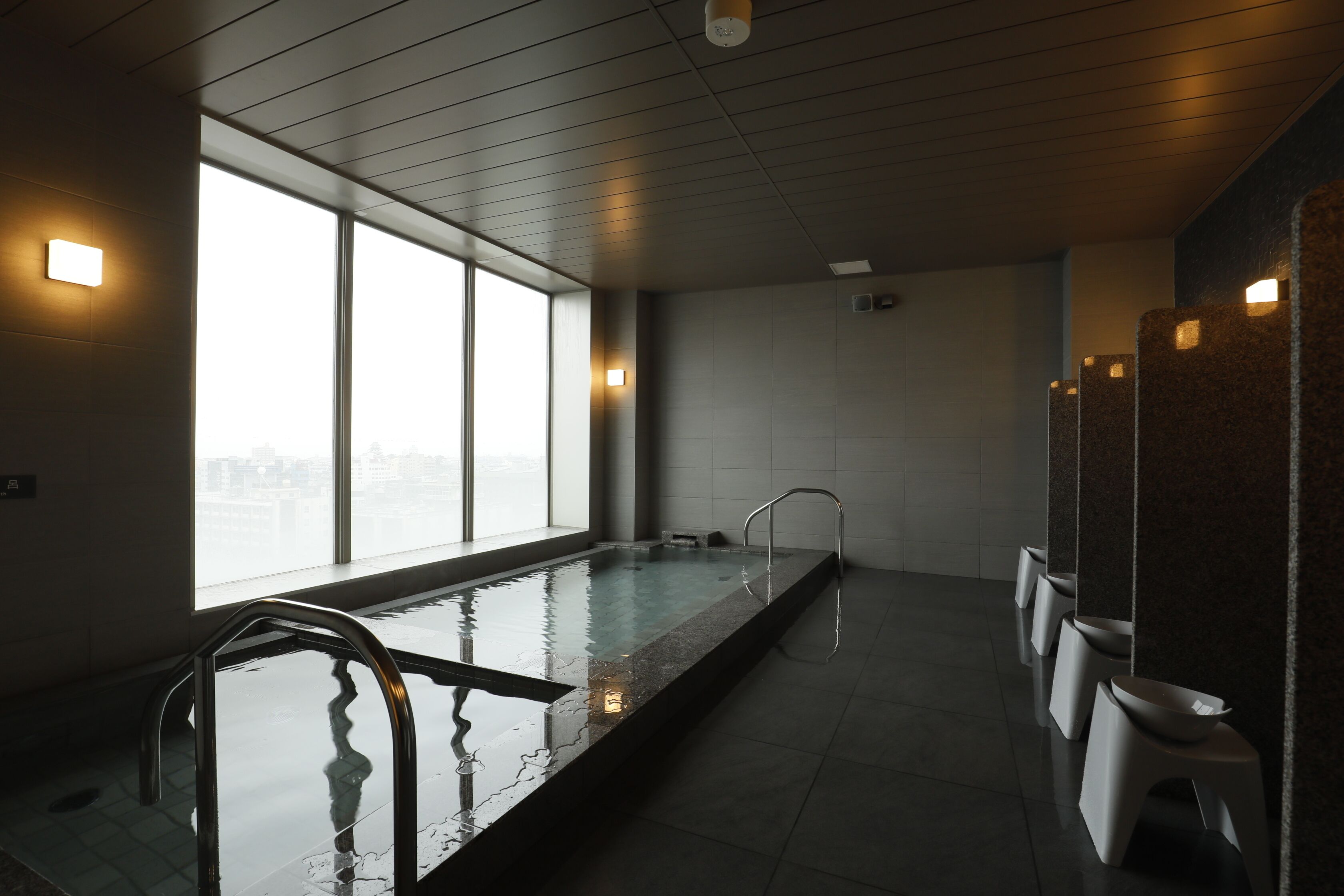 Une piscine intérieure moderne avec des parois en verre transparent, un long banc et une rangée de tabourets blancs.