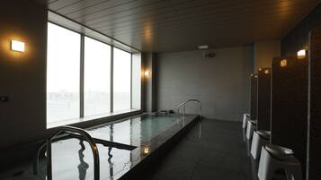 Une piscine intérieure moderne avec des parois en verre transparent, un long banc et une rangée de tabourets blancs.