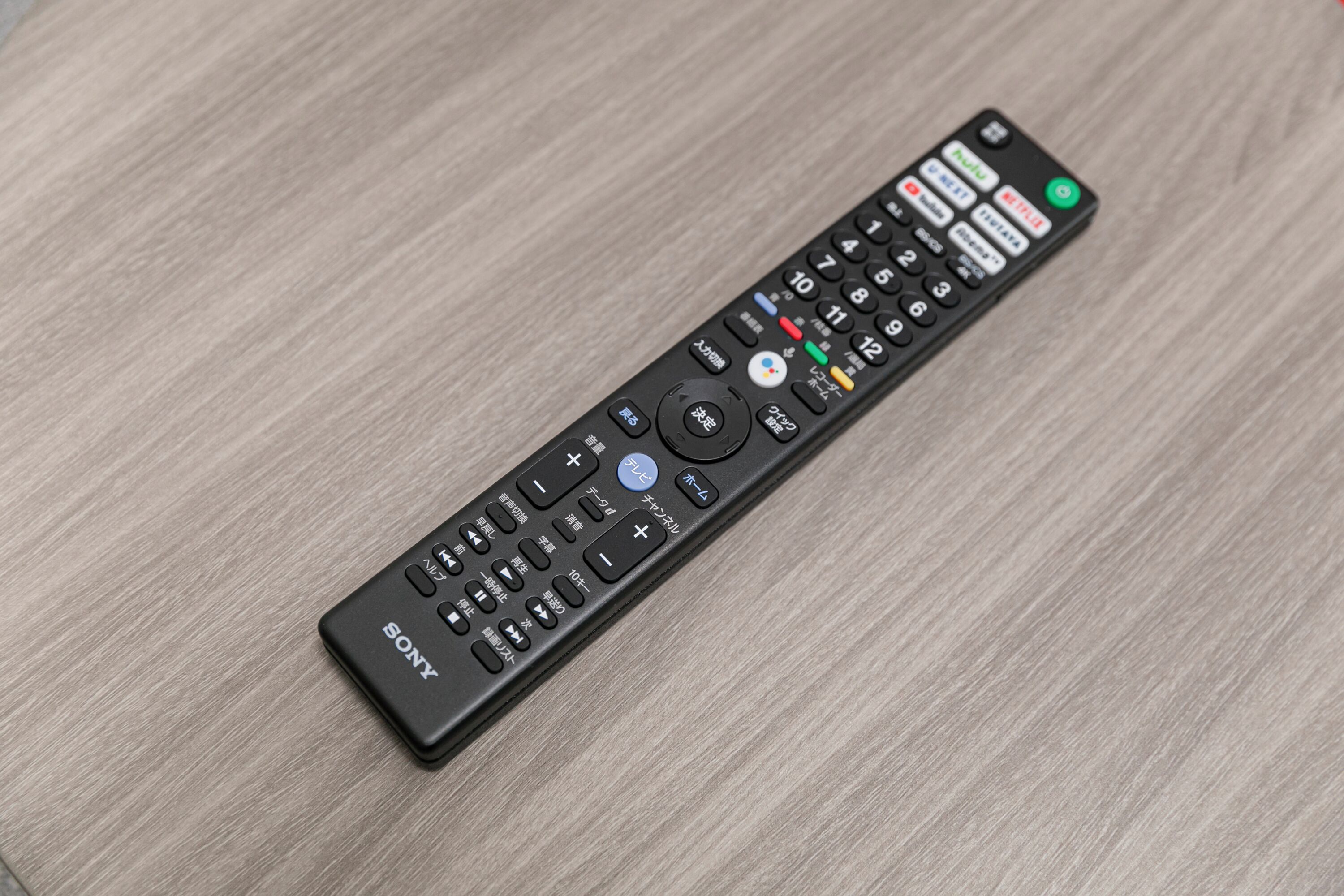 A black remote control with multiple buttons and a Sony logo on a wooden surface.