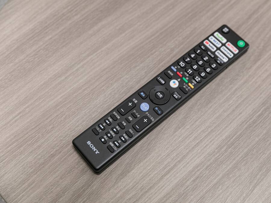 A black remote control with multiple buttons and a Sony logo on a wooden surface.