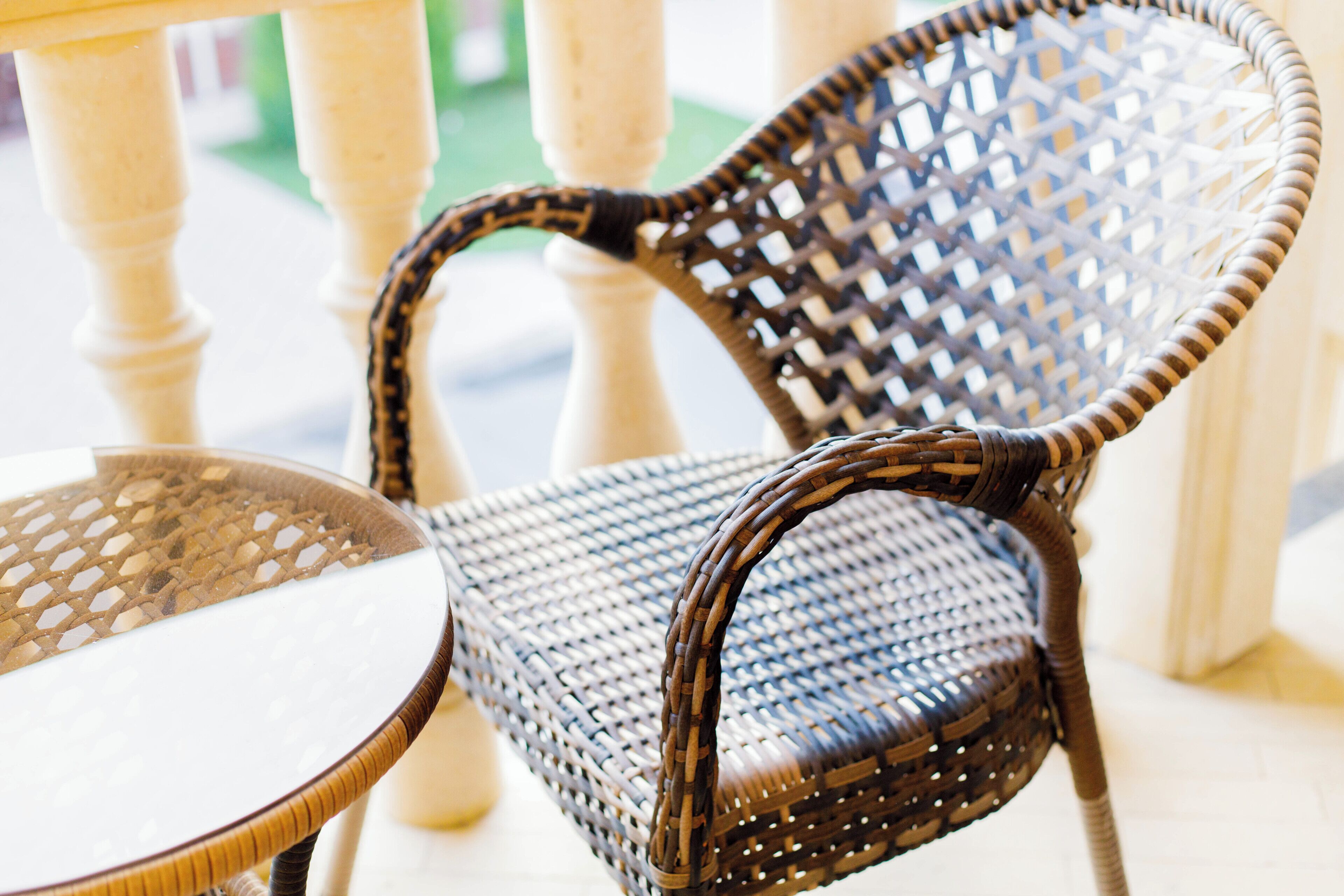A wicker chair with a woven backrest and seat, positioned next to a round table with a glass top.