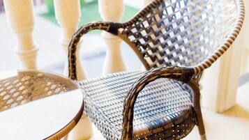 A wicker chair with a woven backrest and seat, positioned next to a round table with a glass top.
