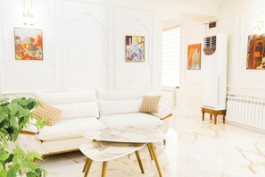 A white sofa with patterned cushions, a marble coffee table, and a radiator in a bright room with artwork on the walls.
