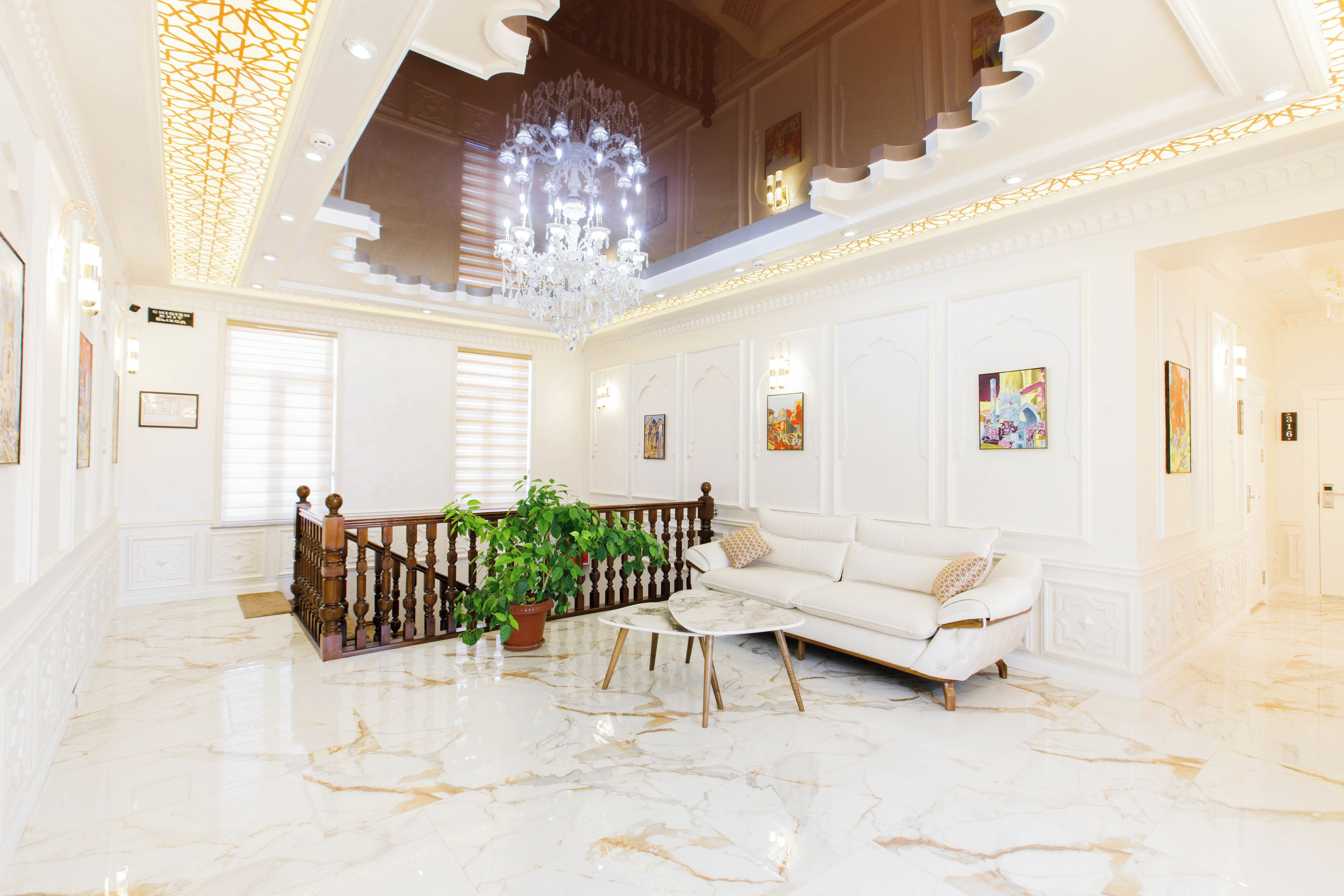 A spacious lobby with a marble floor, a white sofa, a potted plant, a chandelier, and a staircase.
