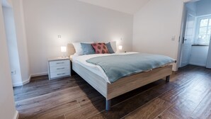 A modern bedroom with a wooden bed, a nightstand, and a bedside lamp. - Gute Auszeit - Ferienwohnung Lichtblick (Borken)