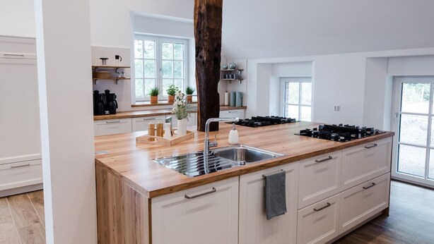 A modern kitchen with a central island, wooden beams, and a large window. - Gute Auszeit - Ferienwohnung Lichtblick (Borken)