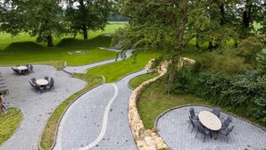 A landscaped outdoor area with curved pathways, stone walls, and outdoor seating arrangements. - Gute Auszeit - Ferienwohnung Lichtblick (Borken)