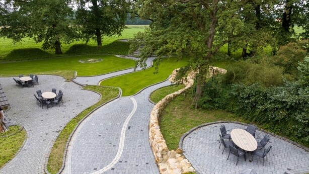 A landscaped outdoor area with curved pathways, stone walls, and outdoor seating arrangements. - Gute Auszeit - Ferienwohnung Weitblick (Borken)