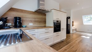 A modern kitchen with white cabinetry, a wooden countertop, and built-in appliances including an oven and a coffee maker. - Gute Auszeit - Ferienwohnung Weitblick (Borken)