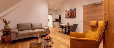 A modern living room with a sofa, armchair, coffee table, and a dining area with chairs and a table.