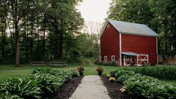 A red barn with a metal roof, surrounded by a garden with a concrete path leading to it. - Historic LaMothe Landing & Farmhouse|SPAC|Track| (Greenfield Center)