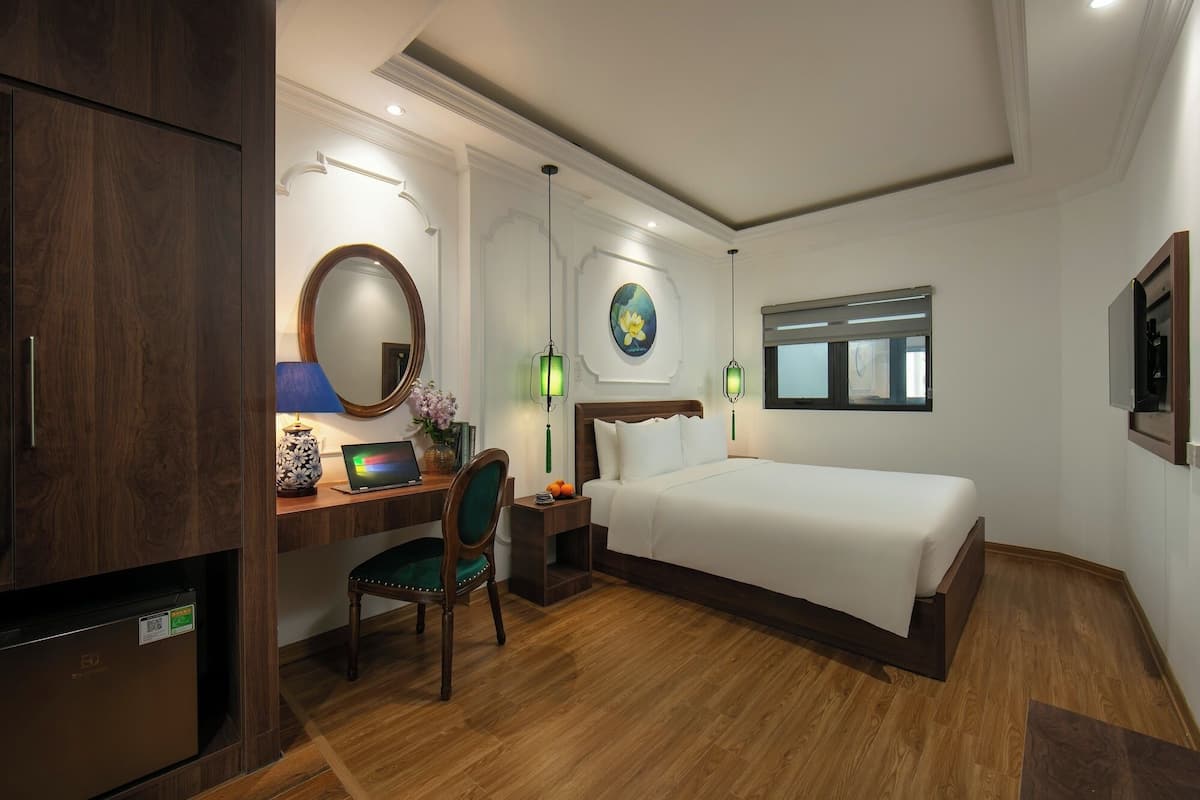 Une chambre d’hôtel avec un bureau en bois, un ordinateur portable, une chaise, un lit et une fenêtre.