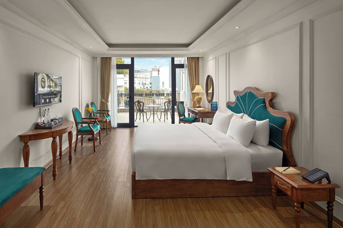 Une chambre d’hôtel avec un grand lit, un bureau, une chaise, une télévision et un balcon offrant une vue sur la ville.