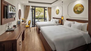 Une chambre d’hôtel avec deux lits, un bureau en bois avec une télévision, une petite table avec un vase, et une vue sur l’extérieur.