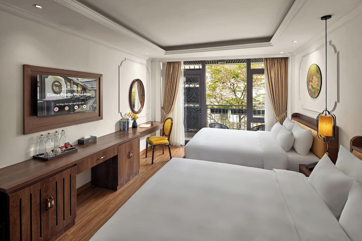 Une chambre d’hôtel avec deux lits, un bureau en bois, une télévision et une grande fenêtre avec des rideaux.