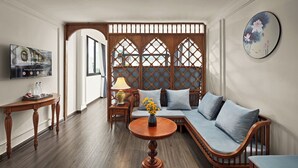 Un salon moderne avec un canapé en bois, une table ronde en bois surmontée d’un vase de fleurs, un téléviseur et un paravent décoratif.