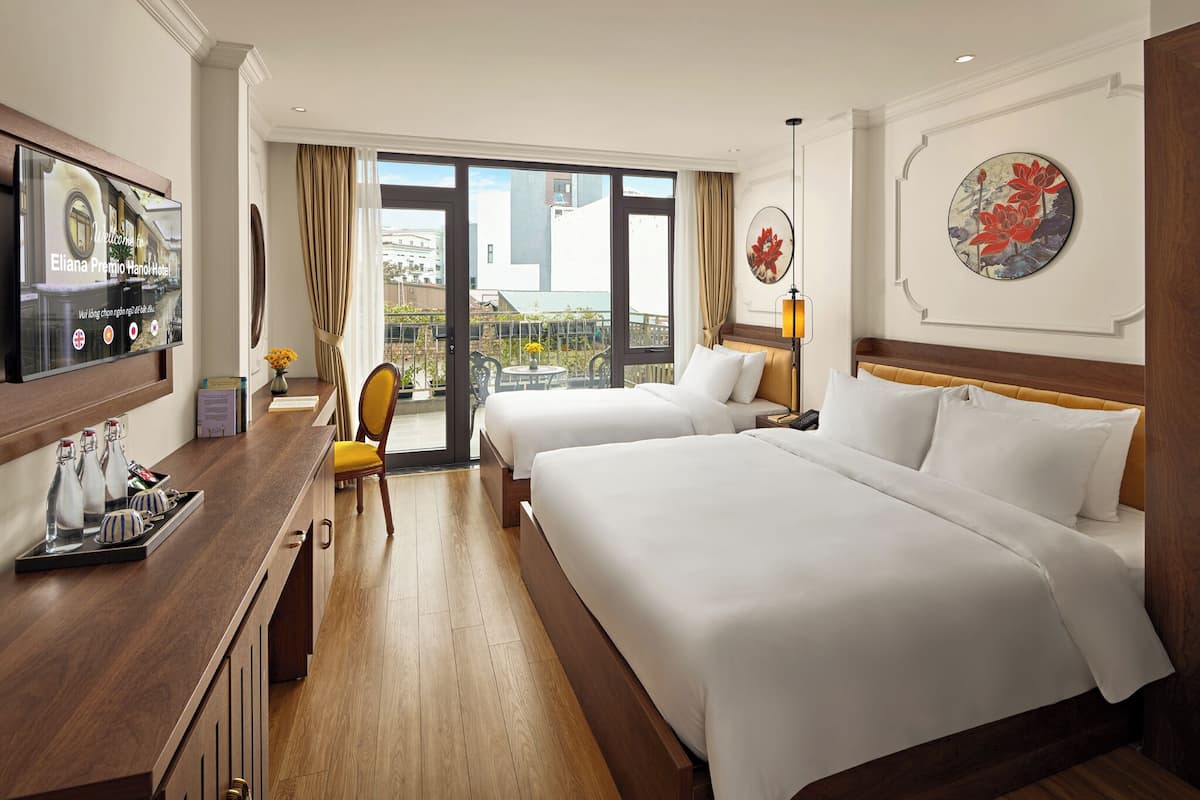 Une chambre d’hôtel avec deux lits, une télévision, un bureau avec un plateau de bouteilles, une chaise et un balcon avec vue.