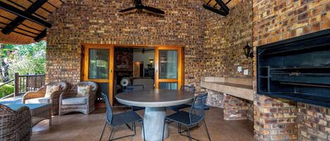 An outdoor patio with a brick wall, a round table with chairs, wicker furniture, and a built-in grill.