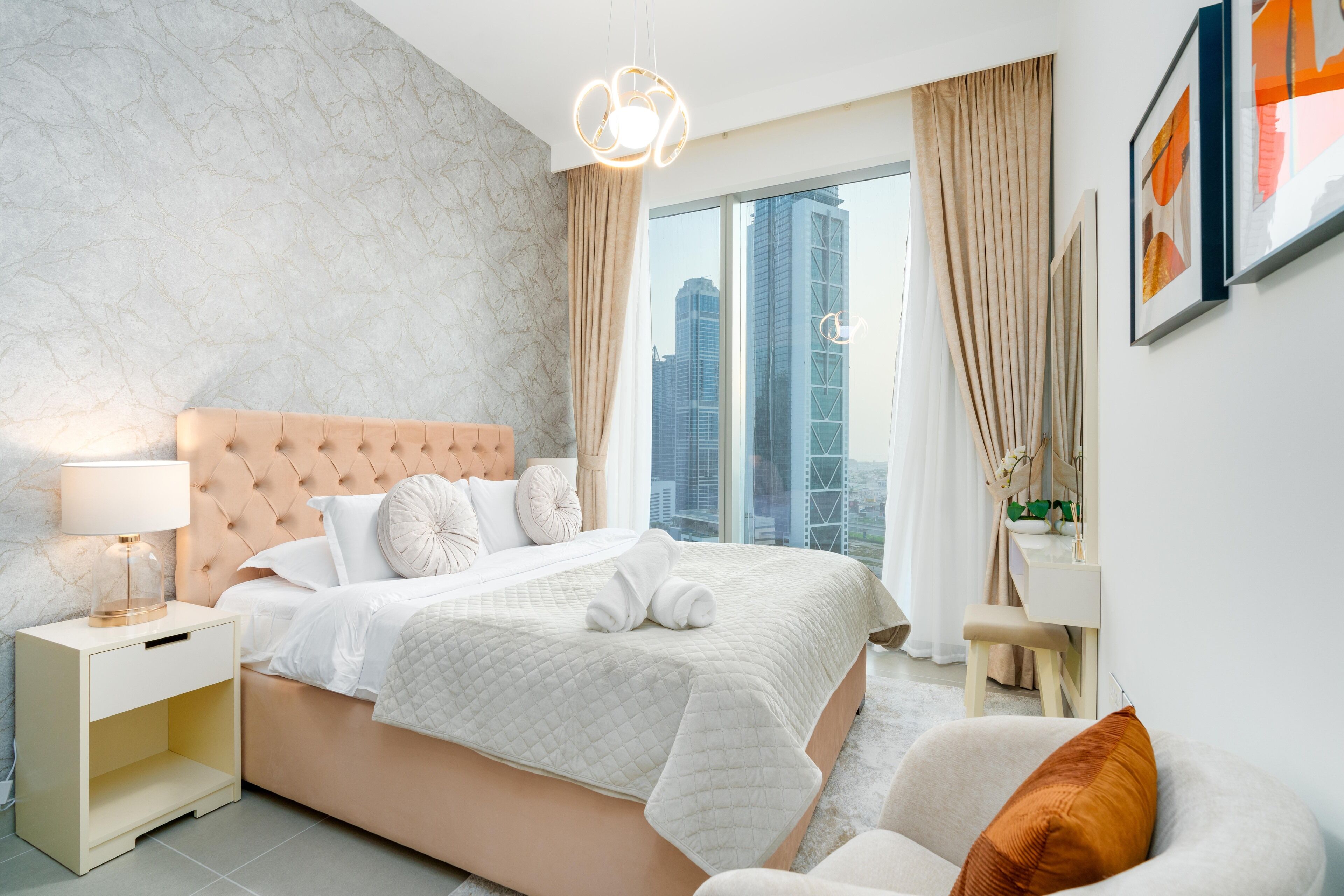 A modern bedroom with a large bed, a nightstand, a chair, and a view of the city.