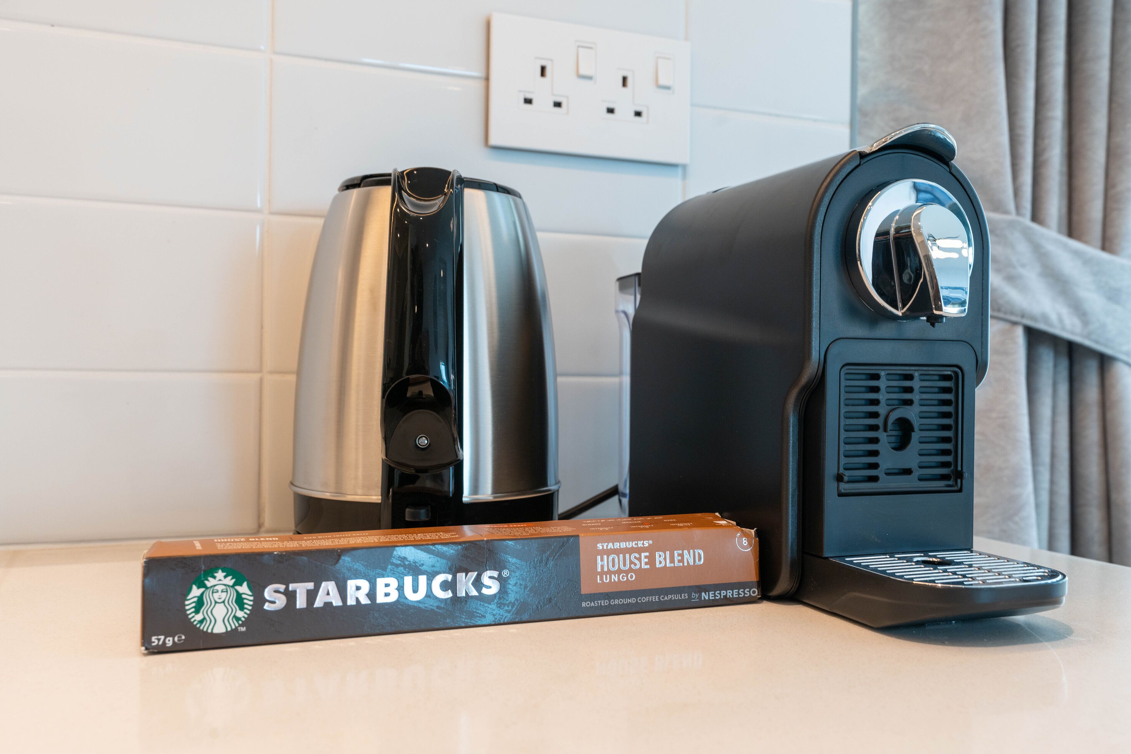 A coffee maker and a box of Starbucks House Blend Lungo coffee capsules on a countertop.