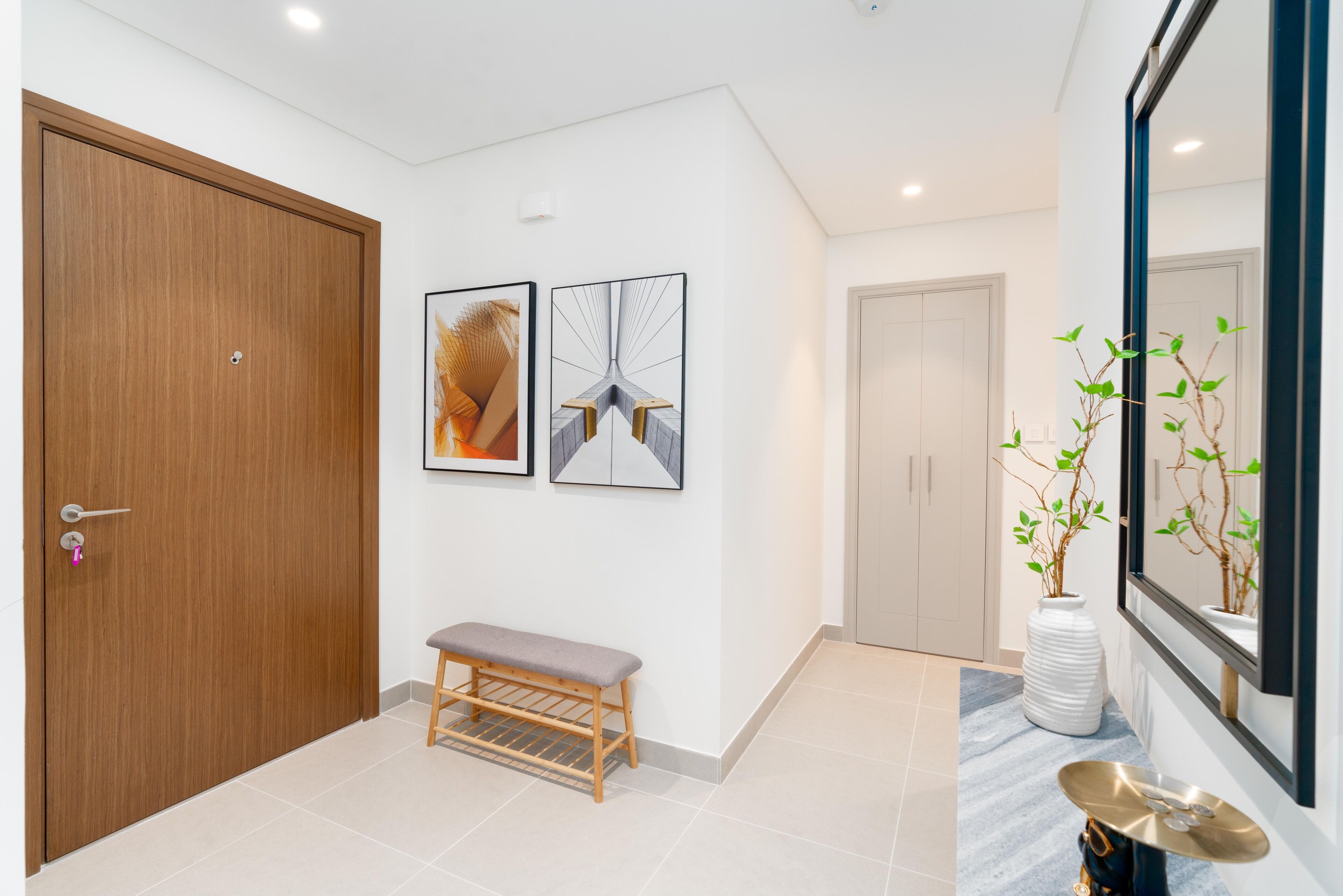 A hallway with a wooden door, a bench, and two framed artworks on the wall.