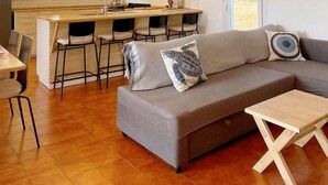 En moderne stue med en grå sofa, et lille træbord og et køkkenområde med barstole.