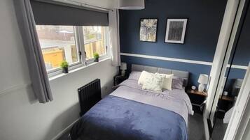 A bedroom with a bed, bedside tables, a radiator, a window with curtains, and artwork on the wall.