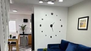 Un salon moderne avec un canapé bleu, une petite table sur laquelle est posée une plante, et une grande horloge murale.