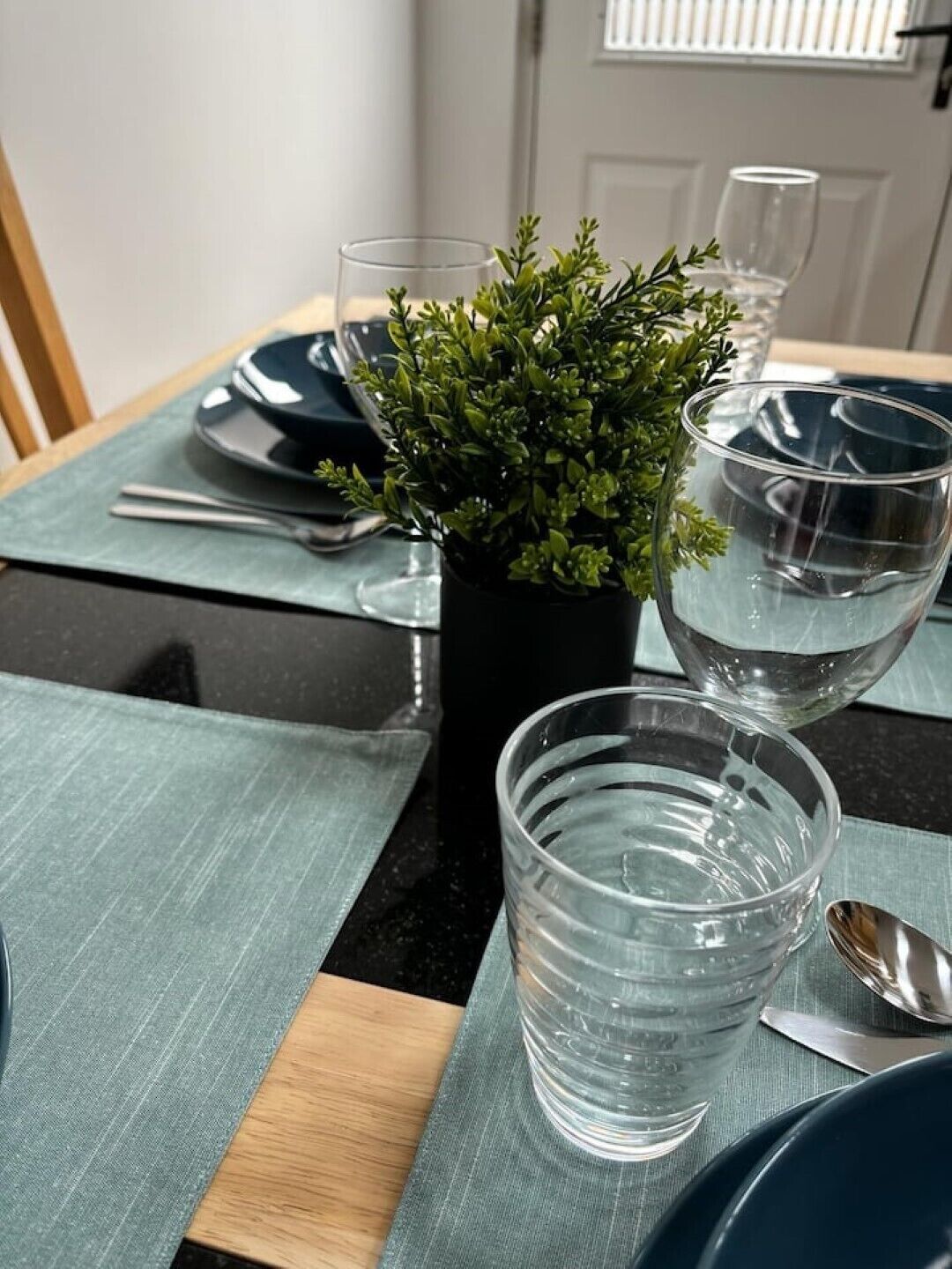 Et spisebord dækket med krystalglas, en potteplante og en blå dug.