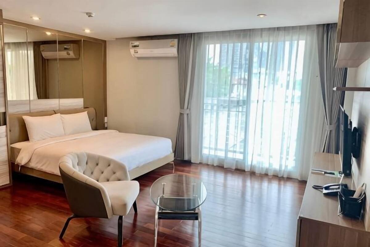 A hotel room with a bed, a chair, a small table, a desk, and a large window with curtains.