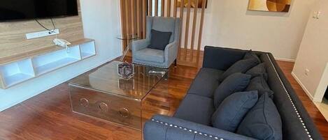 Un salon moderne avec une table basse en verre, un canapé bleu, un fauteuil gris et une cloison en bois.