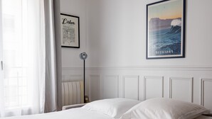 A neatly made bed with white linens and pillows, a framed map of Lisbon, a framed picture of Belharra, and a floor lamp. - The Retro Romantic, by Veeve (Paris)