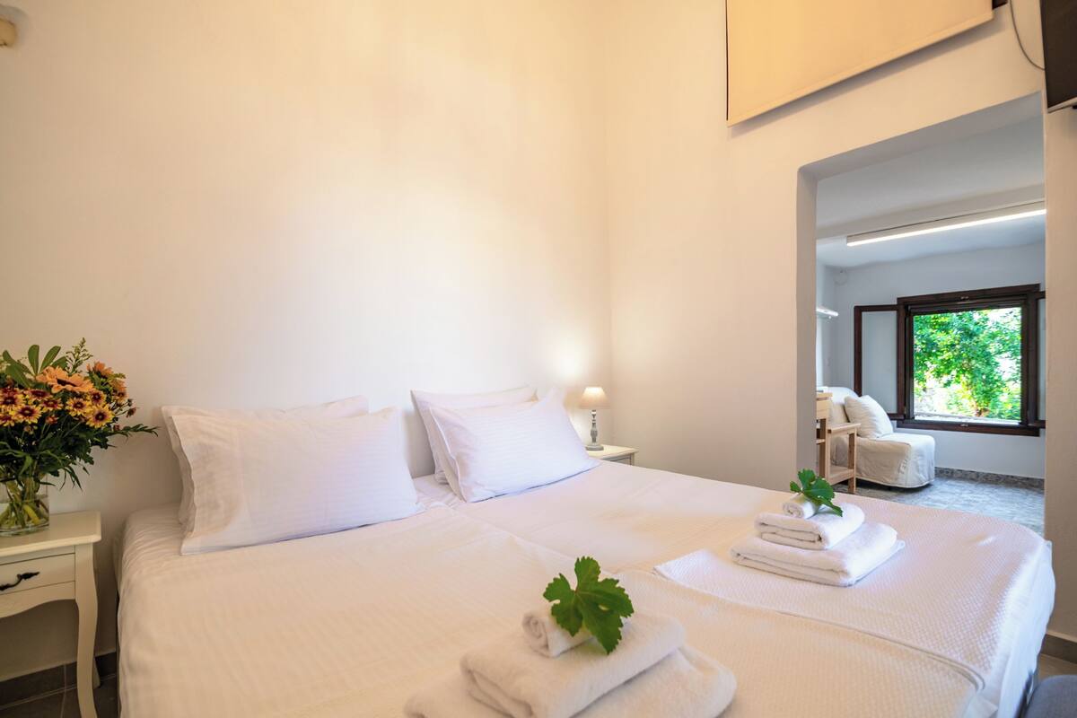 Una habitación de hotel con una cama grande, una mesita de noche con un jarrón de flores y una ventana con vistas a zonas verdes.