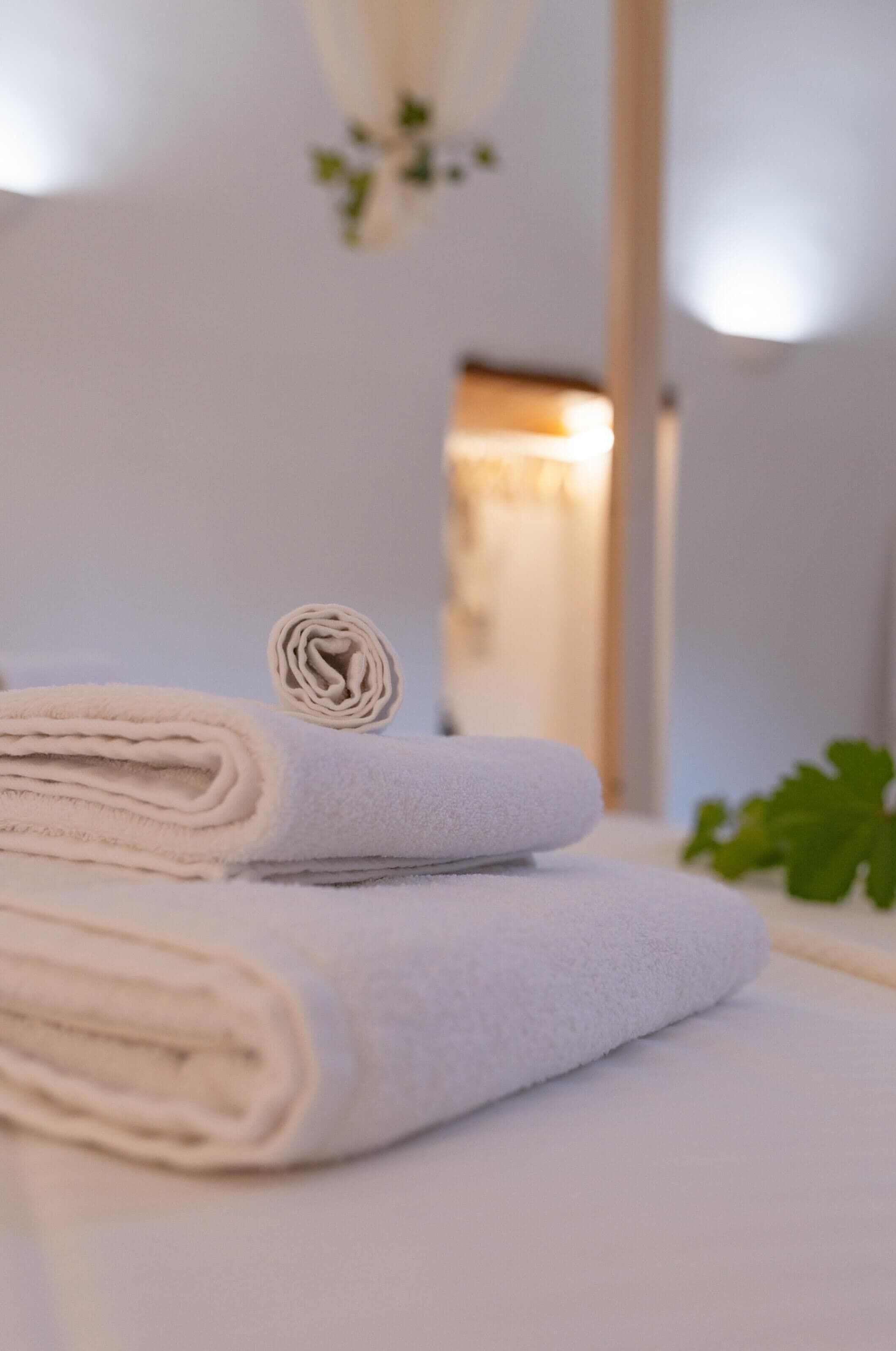 A neatly folded white towel on a bed with a visible door in the background.