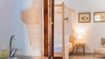 A bedroom with a wooden four-poster bed, a bedside table with a lamp, and a small stool.