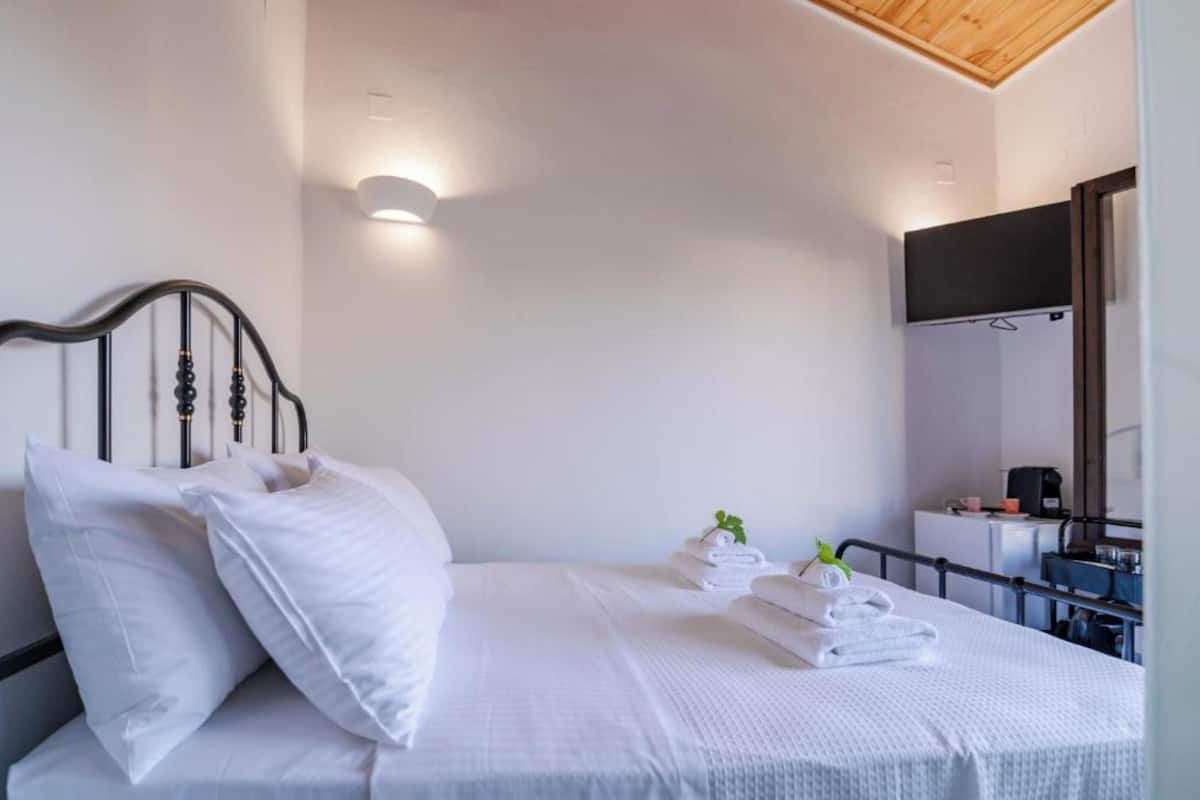 Una cama bien hecha con sábanas y almohadas blancas, una mesita de noche con una planta, y una lámpara de techo moderna.