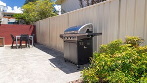 En udendørs terrasse med grill, et bord og stole, samt en rød væg.