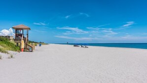 Een strand met een uitkijktoren voor de badmeester, heldere lucht en enkele strandstoelen.