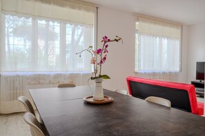 A dining table with chairs, a vase with flowers, and a television in the background.