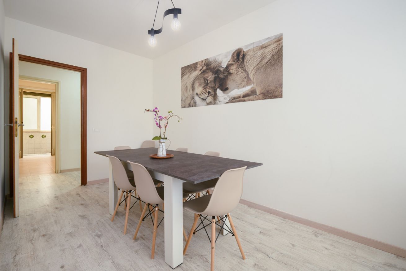 A dining area with a table, chairs, a vase with flowers, and a painting on the wall.