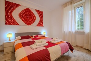 A hotel room with a large bed, two bedside lamps, a window with curtains, and a red and white abstract artwork on the wall.